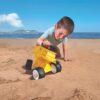 Kinderen spelen met Dump Truck Geel Hape kiepwagen op het strand