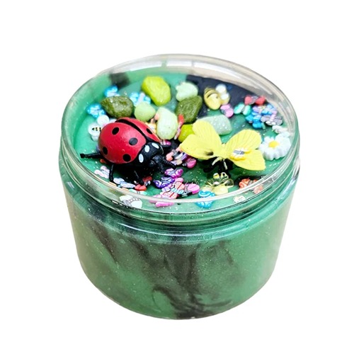 Doosje gevuld met groene sensorische klei, versierd met lieveheersbeestje, bij, kleurrijke steentjes, bloemetjes en kleine vlinders – een vrolijke lentetuin in miniatuurformaat.